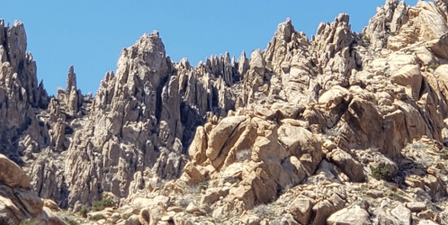 Rocky mountain landscape with jagged peaks and boulders under a clear blue sky.