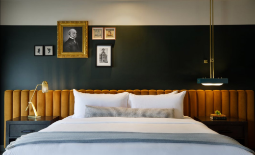 Cozy bedroom featuring a tufted orange headboard, framed art, and modern lighting against a dark wall.