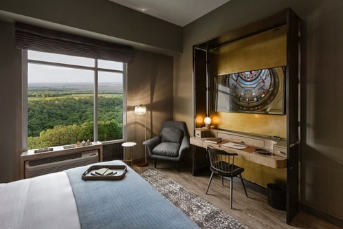 Modern hotel room with a large window showcasing a scenic view, featuring a bed, desk, and cozy seating area.