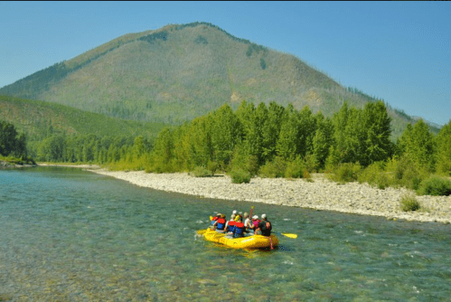 A group of people in a yellow raft navigating a river, surrounded by lush greenery and a mountain in the background.