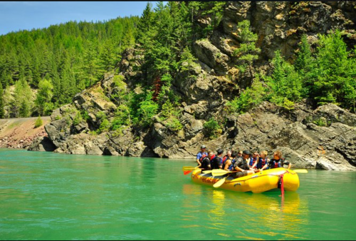 A group of people in a yellow raft on a turquoise river, surrounded by lush green trees and rocky cliffs.