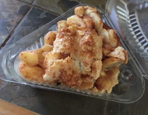A plastic container holding a serving of baked apple dessert with a golden, crispy topping.