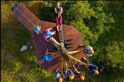 Aerial view of a group of people in helmets preparing for a zip line adventure on a wooden platform in a forested area.