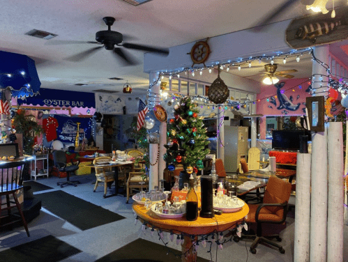 A cozy restaurant interior decorated with holiday lights, a Christmas tree, and colorful seating.