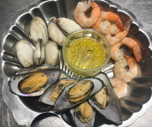 A silver platter with shrimp, clams, mussels, and a small bowl of dipping sauce.