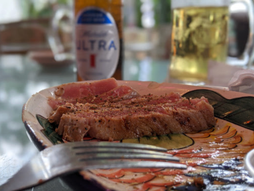 A plate with sliced steak, seasoned and partially eaten, next to a bottle of beer on a table.