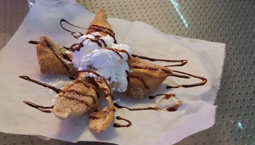 A dessert featuring three crispy pastry triangles topped with whipped cream and drizzled with chocolate sauce.