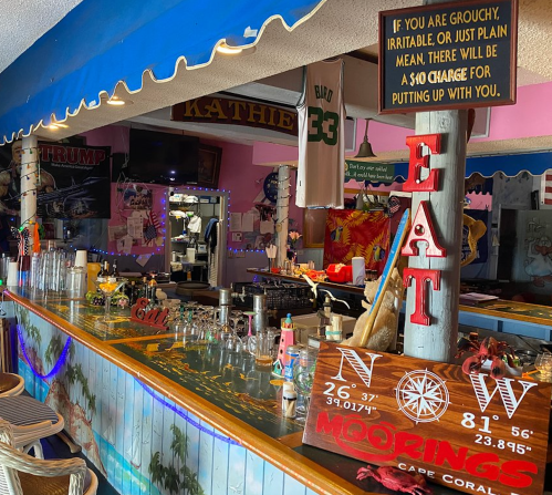 A colorful bar interior with a "EAT" sign, tropical decor, and a playful warning about service charges.