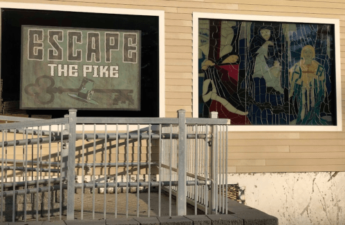 Sign reading "Escape the Pike" next to colorful stained glass windows on a building exterior.