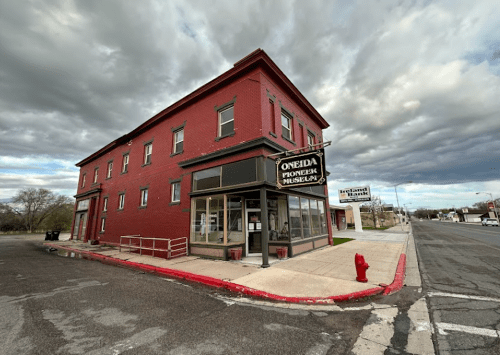 Red brick building with "Oneida Pioneers Museum" sign, cloudy sky, and street view in a small town.