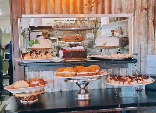 A display of various cakes and pastries on plates, set against a rustic kitchen backdrop.