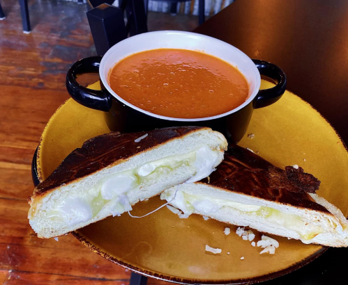 A plate with a grilled cheese sandwich, cut in half, and a bowl of tomato soup.