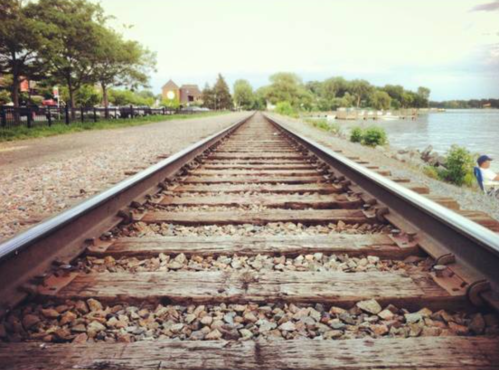 A view of railway tracks stretching into the distance, flanked by greenery and a body of water.