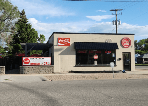 A small pizza restaurant with a Coca-Cola sign, outdoor seating, and an "Open" sign on a sunny day.