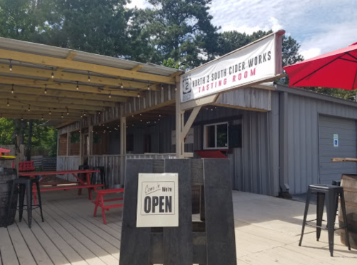 A rustic cider tasting room with outdoor seating, featuring a sign that says "We're OPEN" in front.
