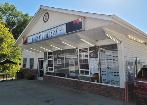 A small ice cream shop with a sign reading "Man Freeze," featuring large windows and outdoor seating.