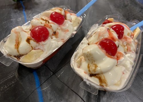 Two plastic containers filled with banana splits topped with whipped cream, chocolate syrup, and cherries.