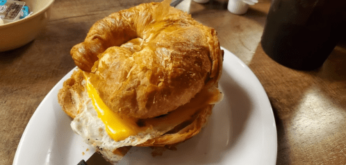 A toasted croissant sandwich with melted cheese and a fried egg, served on a white plate.