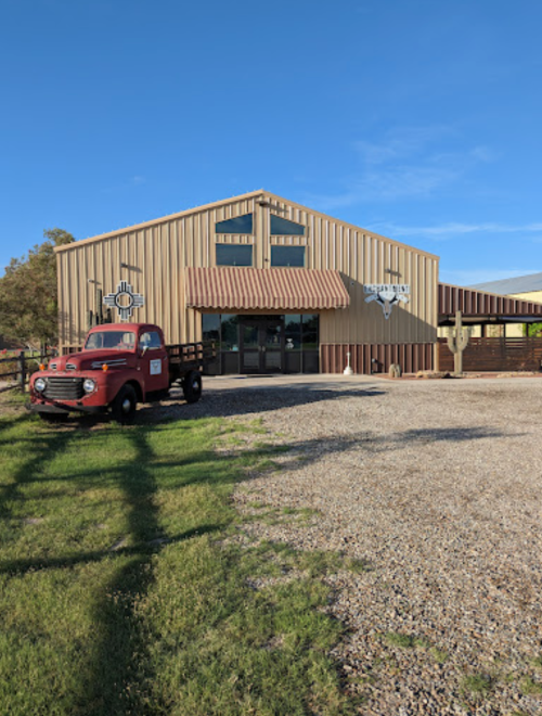 A rustic building with a metal exterior, featuring a vintage red truck parked in front on a gravel driveway.