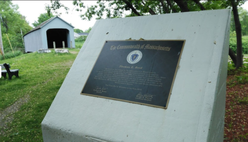Plaque honoring Thomas E. Reed, with a historic building and greenery in the background.
