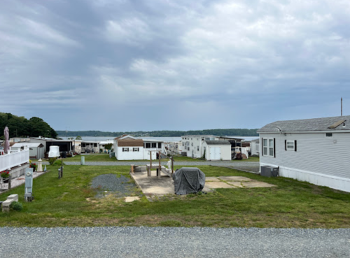 A view of a mobile home park with several homes, a grassy area, and a cloudy sky in the background.