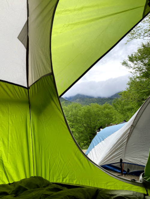 View from inside a green tent, showing a misty mountain landscape and another blue tent outside.