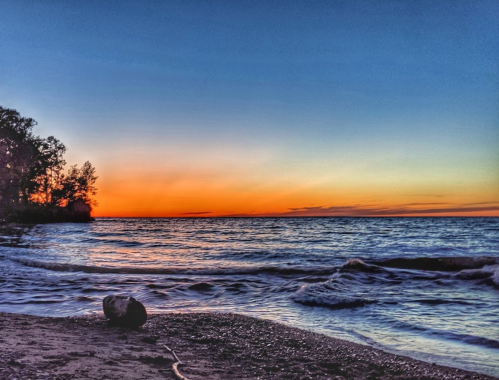 A serene beach at sunset, with calm waves and a colorful sky transitioning from orange to blue.