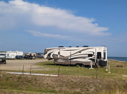 A large RV parked in a gravel area with other RVs in the background and a blue sky above.