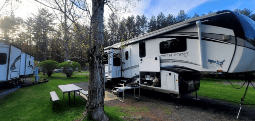 A North Point RV parked in a campsite surrounded by trees, with a picnic table and grill nearby.
