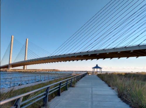 A modern cable-stayed bridge spans over a waterway, with a gazebo and pathway in the foreground.