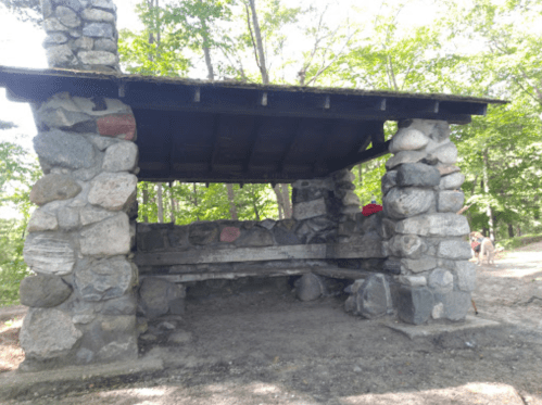 Stone shelter with a wooden bench, surrounded by trees in a natural setting.