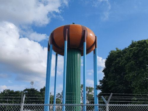 A colorful water tower designed to look like a pumpkin, surrounded by trees and a blue sky.