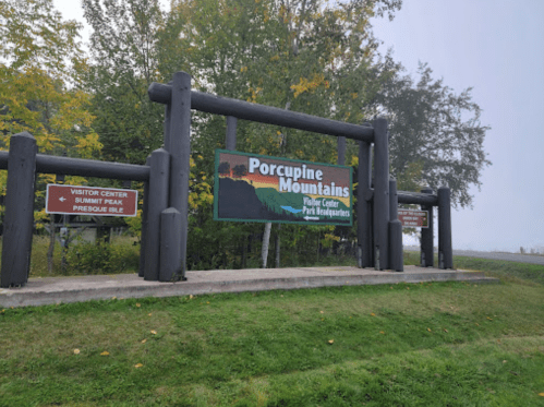 Sign for Porcupine Mountains Visitor Center and Park Headquarters, surrounded by trees in a foggy setting.