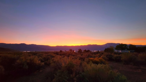 A serene sunset over mountains, with vibrant orange and purple hues illuminating the sky above a lush landscape.