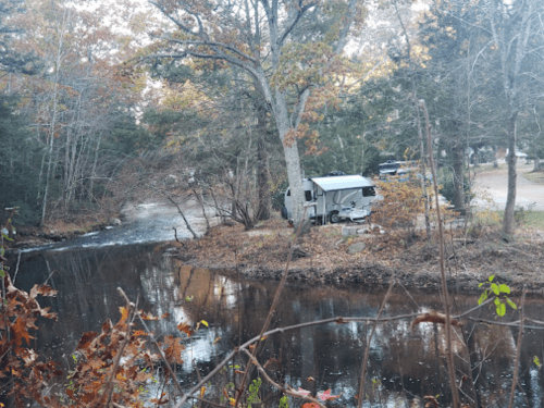 A camper parked by a serene river surrounded by trees in a peaceful outdoor setting.