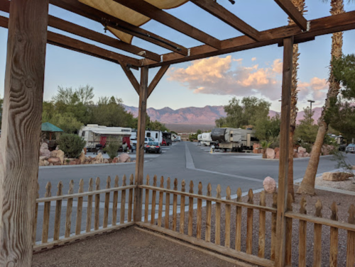 View from a wooden pergola overlooking a campground with RVs and mountains in the background under a clear sky.