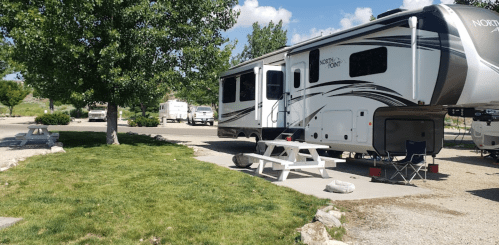 A spacious RV park with several RVs, picnic tables, and green grass under a blue sky with scattered clouds.