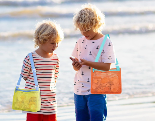 Two young boys at the beach, one wearing a striped shirt and the other in a patterned tee, both holding small items.