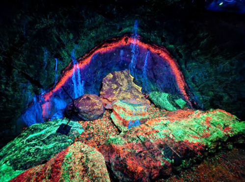 A vibrant cave interior with colorful rock formations and glowing mineral patterns illuminated in various hues.