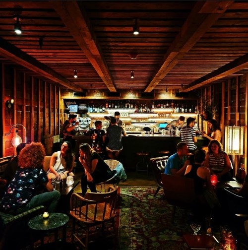 A cozy bar scene with patrons socializing, dim lighting, wooden decor, and a well-stocked bar in the background.