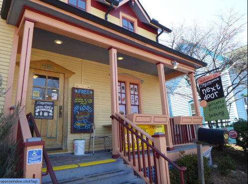 A charming yellow house with a porch, featuring a sign for a dessert shop called "Next Door" and a delivery notice.