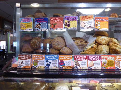 A display case filled with various baked goods, including muffins, scones, and cookies, with price tags visible.