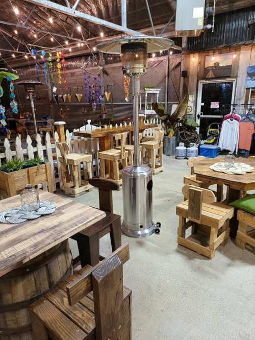 A cozy indoor space featuring wooden tables, chairs, and a patio heater, with decorative items hanging in the background.