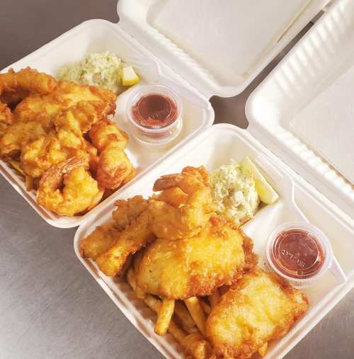Two takeout containers filled with fried seafood, including shrimp and fish, accompanied by sauces and sides.