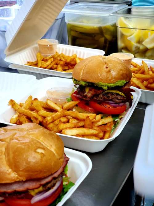 Two burgers with lettuce, tomato, and sauces, served with a side of golden fries in takeout containers.