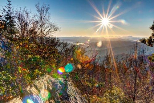 A scenic mountain view at sunrise, with vibrant colors and lens flare effects illuminating the landscape.