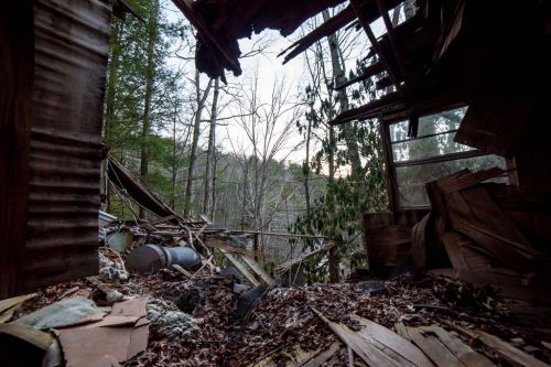 View from inside a dilapidated structure, showing fallen debris and trees outside in a wooded area.