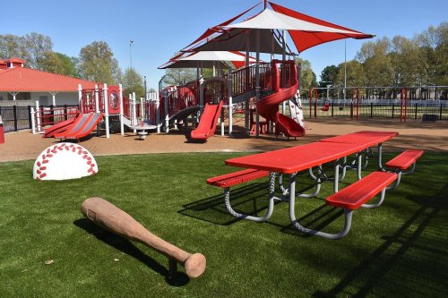 Colorful playground with slides, picnic tables, and a baseball-themed design on a grassy area.