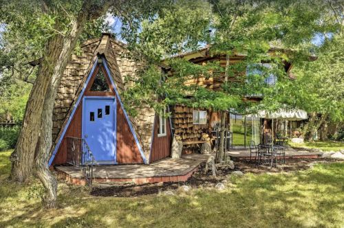 A unique, triangular-shaped house with a blue door, surrounded by trees and a grassy area.