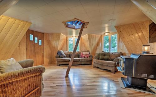 Cozy living room with wooden walls, a unique central support beam, and large windows letting in natural light.